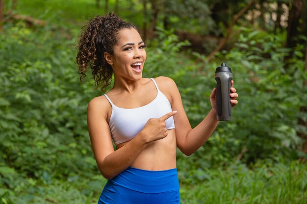 Young afro woman in the park holding a bottle of water.