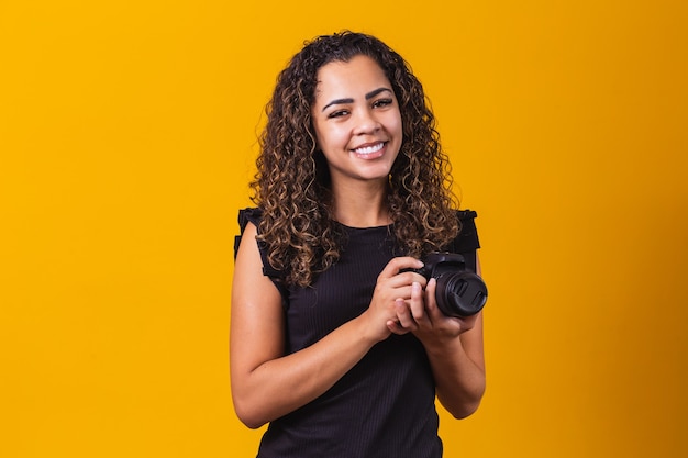 Young afro woman photography on yellow background holding a photo camera.