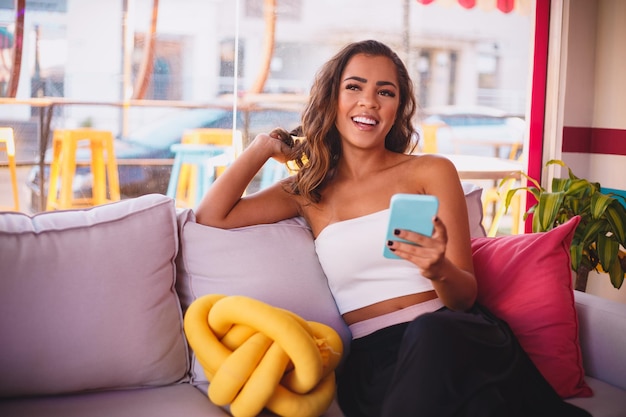 Young afro woman sitting on sofa using cellphone at home