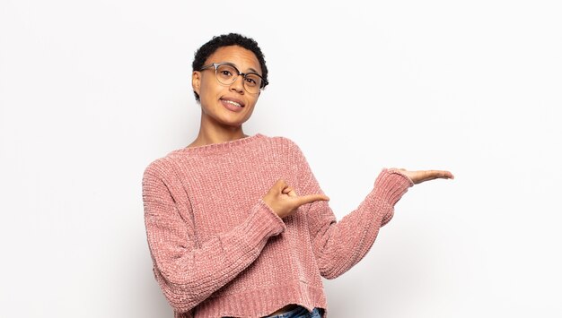 Young afro woman smiling, feeling happy, carefree and satisfied, pointing to concept or idea on copy space on the side