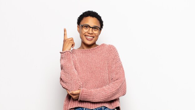 Young afro woman smiling happily and looking sideways, wondering, thinking or having an idea