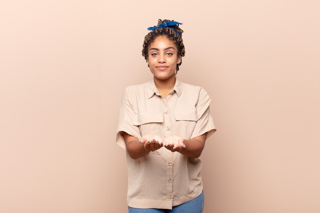 Photo young afro woman smiling happily with friendly, confident, positive look, offering and showing an object or concept