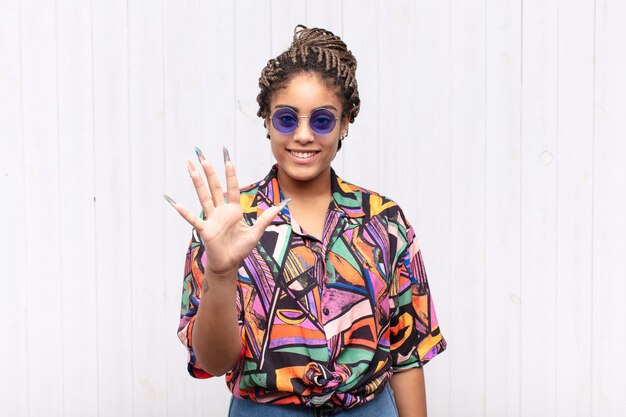 Giovane donna afro sorridente e guardando amichevole, mostrando il numero cinque o quinto con la mano in avanti, il conto alla rovescia