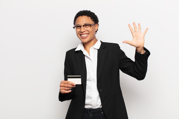 Young afro woman smiling and looking friendly, showing number five or fifth with hand forward, counting down