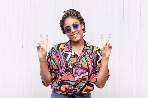 Young afro woman smiling and looking happy, friendly and satisfied, gesturing victory or peace with both hands