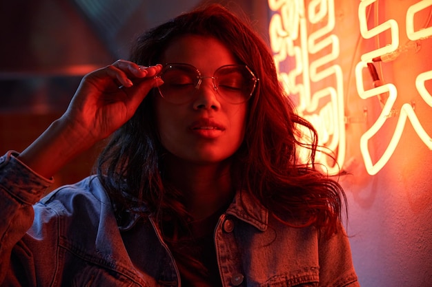 Photo young afro woman wears trendy glasses stands in red neon sign night club light