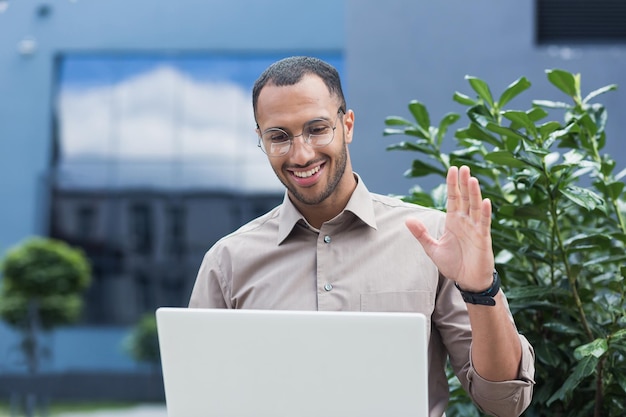 Young afroamerican student using laptop for video call businessman outside office building smiling