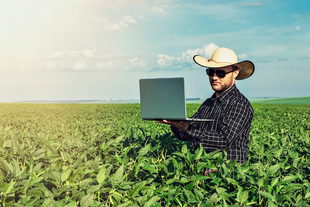 Young agronomist in hat holding  notebook in soybean field.