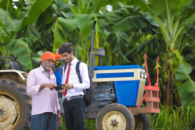 Молодой агроном показывает некоторую информацию на планшете индийскому фермеру