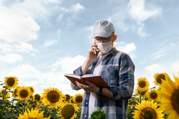 Young agronomist with face mask working in sunflower field