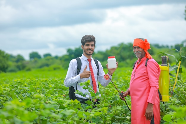 Молодой агроном с фермером показывает бутылку удобрений в поле