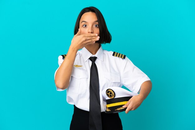 Young airplane pilot over isolated blue background covering mouth with hands