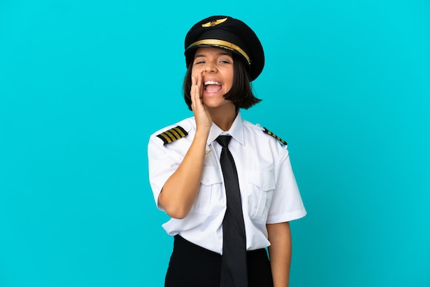 Young airplane pilot over isolated blue background shouting with mouth wide open