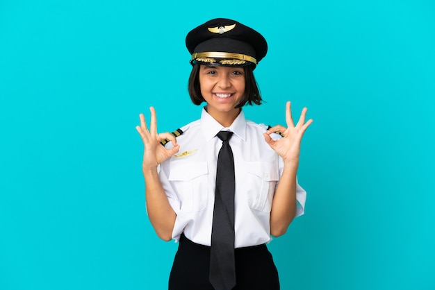 Young airplane pilot over isolated blue background showing ok sign with two hands