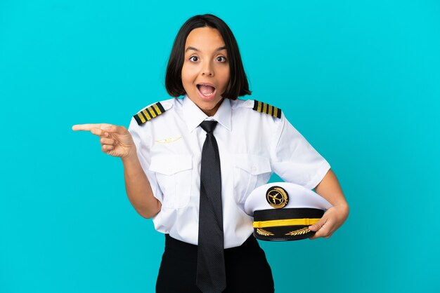 Young airplane pilot over isolated blue background surprised and pointing side