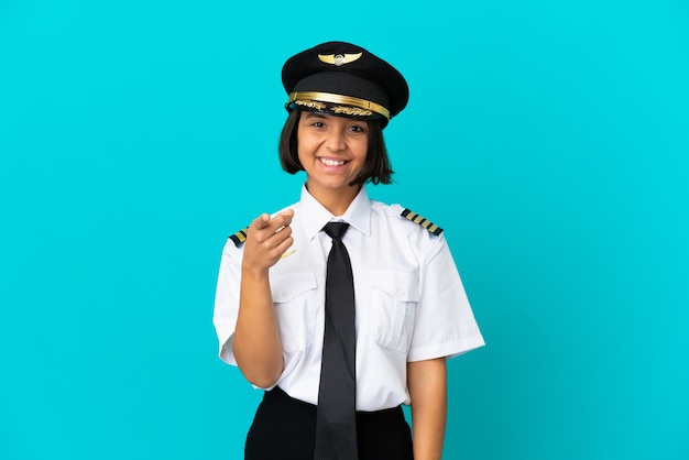 Young airplane pilot over isolated blue wall pointing front with happy expression