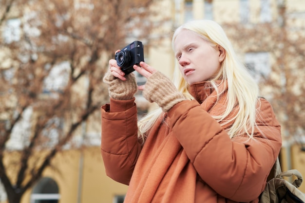 Young albino woman with photocamera taking photos of autumn city