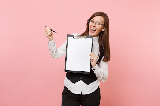 Young amazed business woman in glasses pointing pen on clipboard tablet with blank empty sheet workspace copy space isolated on pink background. Lady boss. Achievement career wealth. Advertising area.