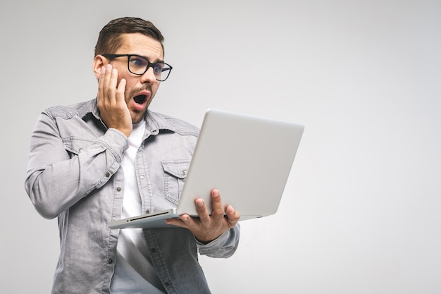 Young amazed emotional brunet with bristle with sad grimace looks at screen of device