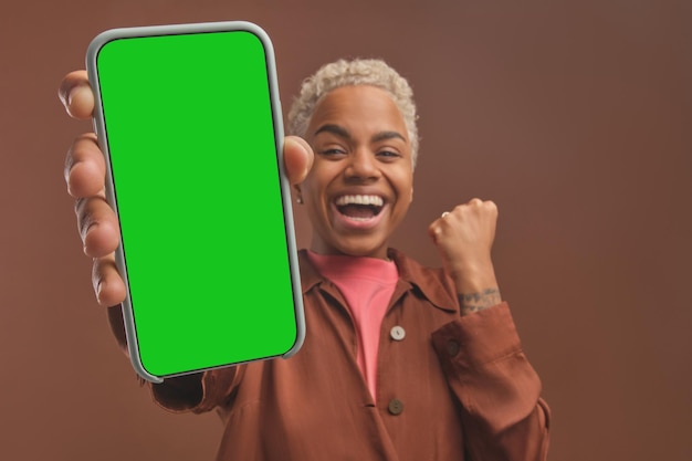 Young amazed happy african american woman with phone makes victory gesture