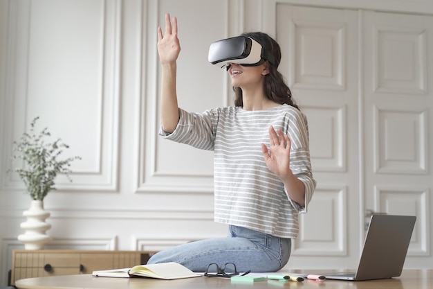 Молодая пораженная женщина-сотрудник в очках гарнитуры VR пытается прикоснуться к чему-то в виртуальной реальности