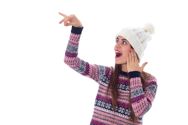 Young amazed woman in white hat and purple sweater holding something on white background in studio