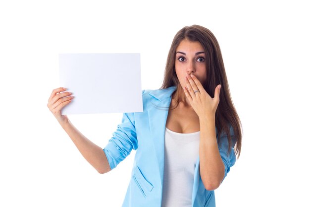 Young amazed woman in white Tshirt and jeans holding white sheet of paper and looking on it