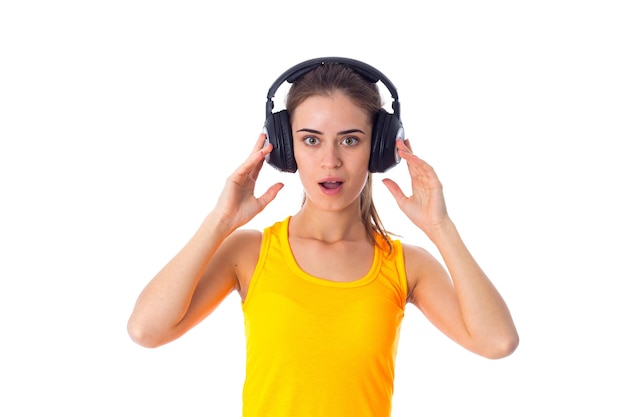 Young amazed woman with ponytail in yellow T-shirt and black headphones on white background in studio