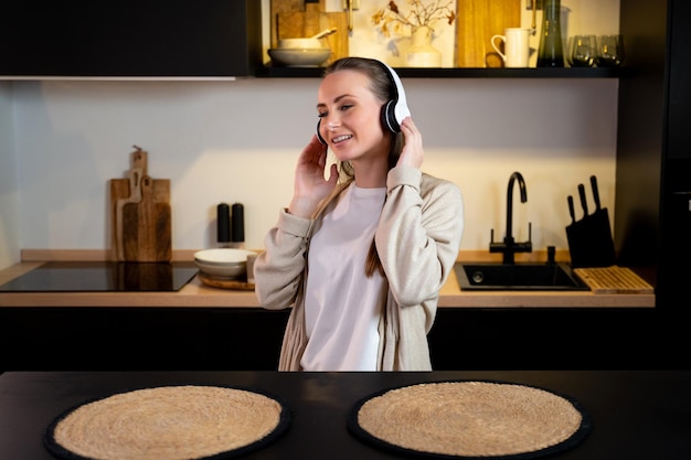 Young amazing emotional woman dancing in the kitchen indoors at home listening to music with headpho