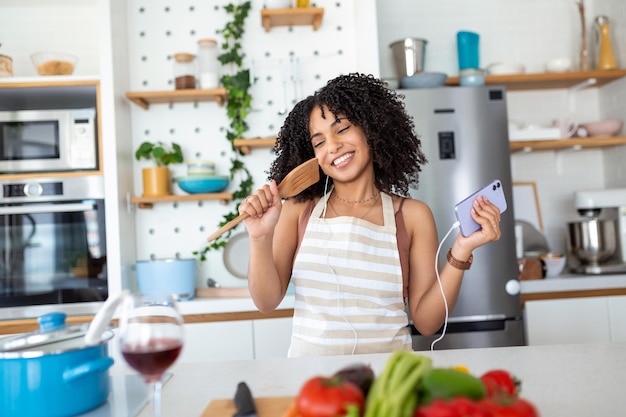 Young amazing emotional woman dancing in kitchen indoors at home listening music with headphones cooking