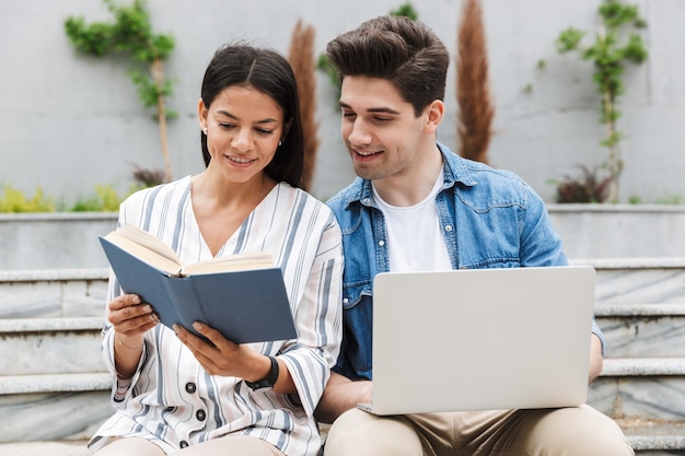 young amazing loving couple business people colleagues outdoors outside on steps using laptop computer reading book.