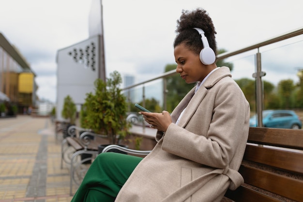 Young american woman listening to music with headphones on the phone against the backdrop of a city