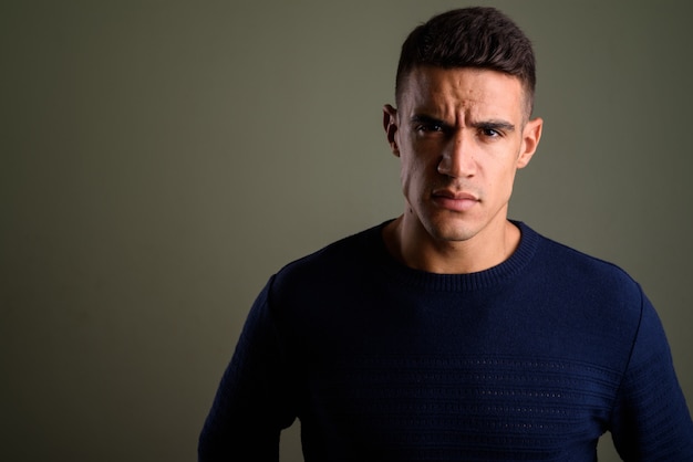 Young angry man wearing sweater against colored background