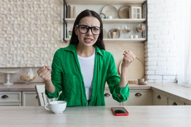 Young angry woman talking on video call angry and looking at camera brunette at home in kitchen