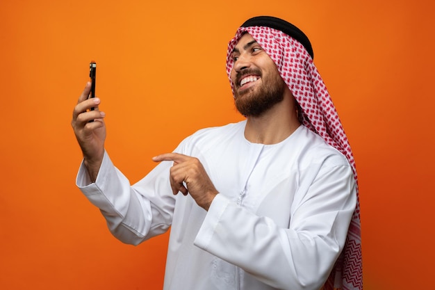 Young Arab businessman using smartphone on orange background