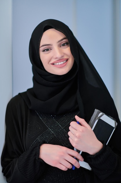 전통적인 옷을 입은 젊은 아랍 여성 사업가나 현대 이슬람 패션 기술을 나타내는 검은 칠판 앞에 태블릿 컴퓨터가 있는 아바야