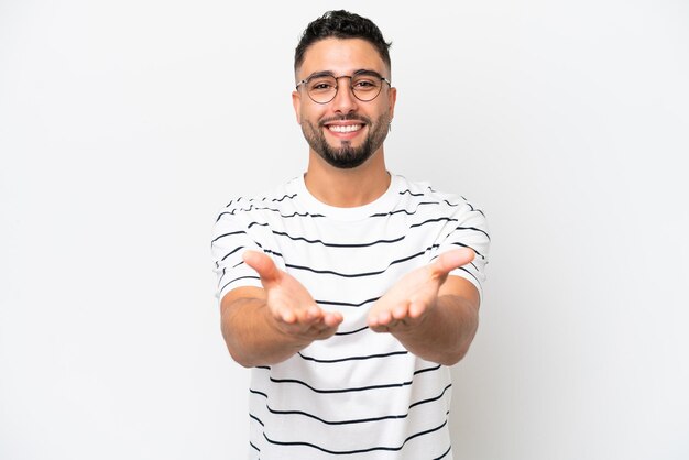 Young Arab handsome man isolated on white background holding copyspace imaginary on the palm to insert an ad