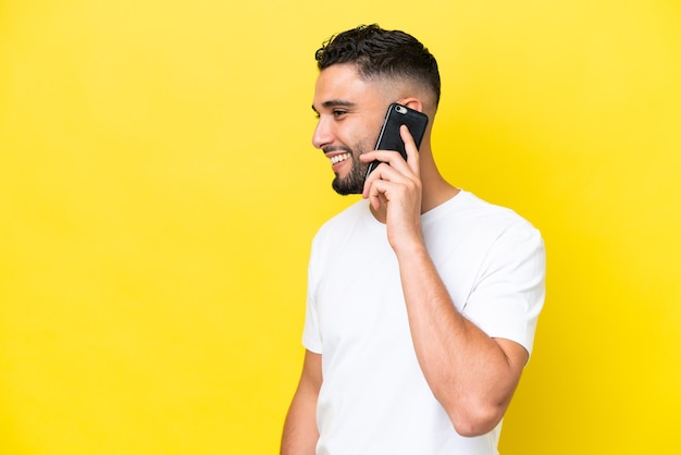 Young Arab handsome man isolated on yellow background keeping a conversation with the mobile phone with someone