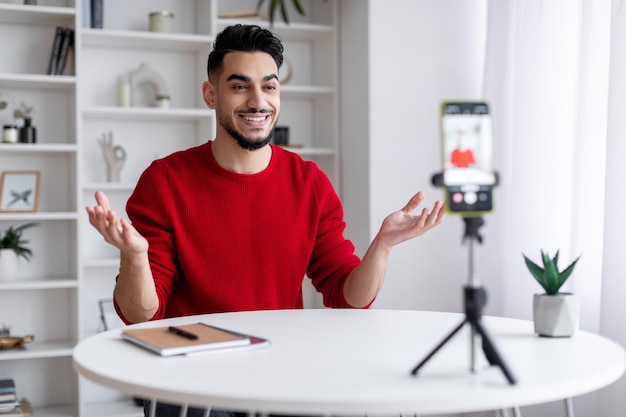 三脚にスマートフォンを使って自宅でビデオを録画する若いアラブの男性ブロガー