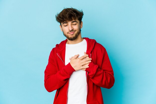 Young arab man on blue has friendly expression, pressing palm to chest. Love concept.