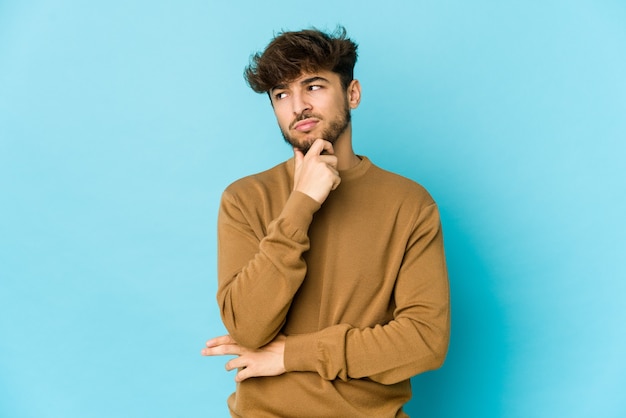 Young arab man on blue thinking and looking up, being reflective, contemplating, having a fantasy.