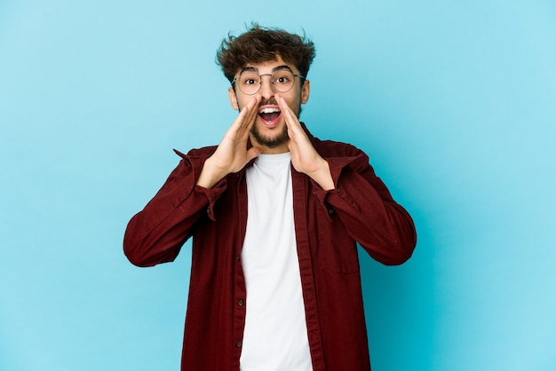 Young arab man on blue wall saying a gossip, pointing to side reporting something.