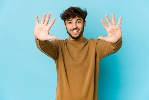 Young arab man on blue wall, showing number ten with hands.