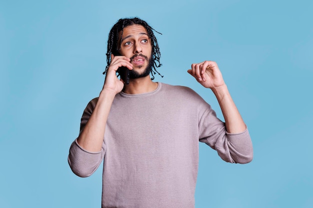 Young arab man chatting on mobile phone while explaining thoughts and gesticulating with hands. handsome person in casual clothes answering call, having conversation on smartphone