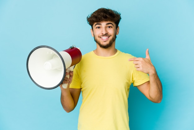 Young arab man holding a megaphone person pointing by hand to a shirt copy space, proud and confident