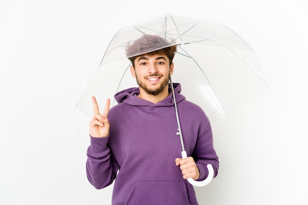 Young arab man holding an umbrella showing number two with fingers.