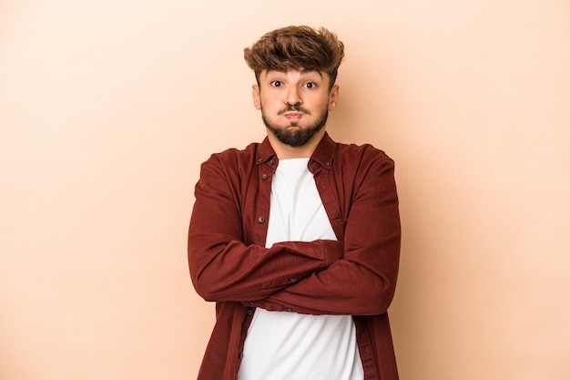 Young arab man isolated on beige background blows cheeks, has tired expression. Facial expression concept.