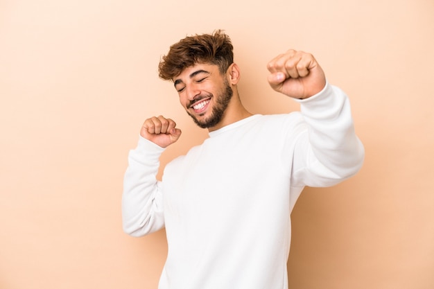 Young arab man isolated on beige background celebrating a special day, jumps and raise arms with energy.