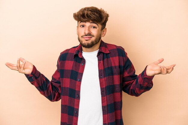 Young arab man isolated on beige background doubting and shrugging shoulders in questioning gesture.