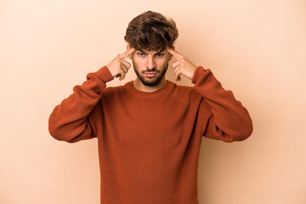 Young arab man isolated on beige background focused on a task, keeping forefingers pointing head.